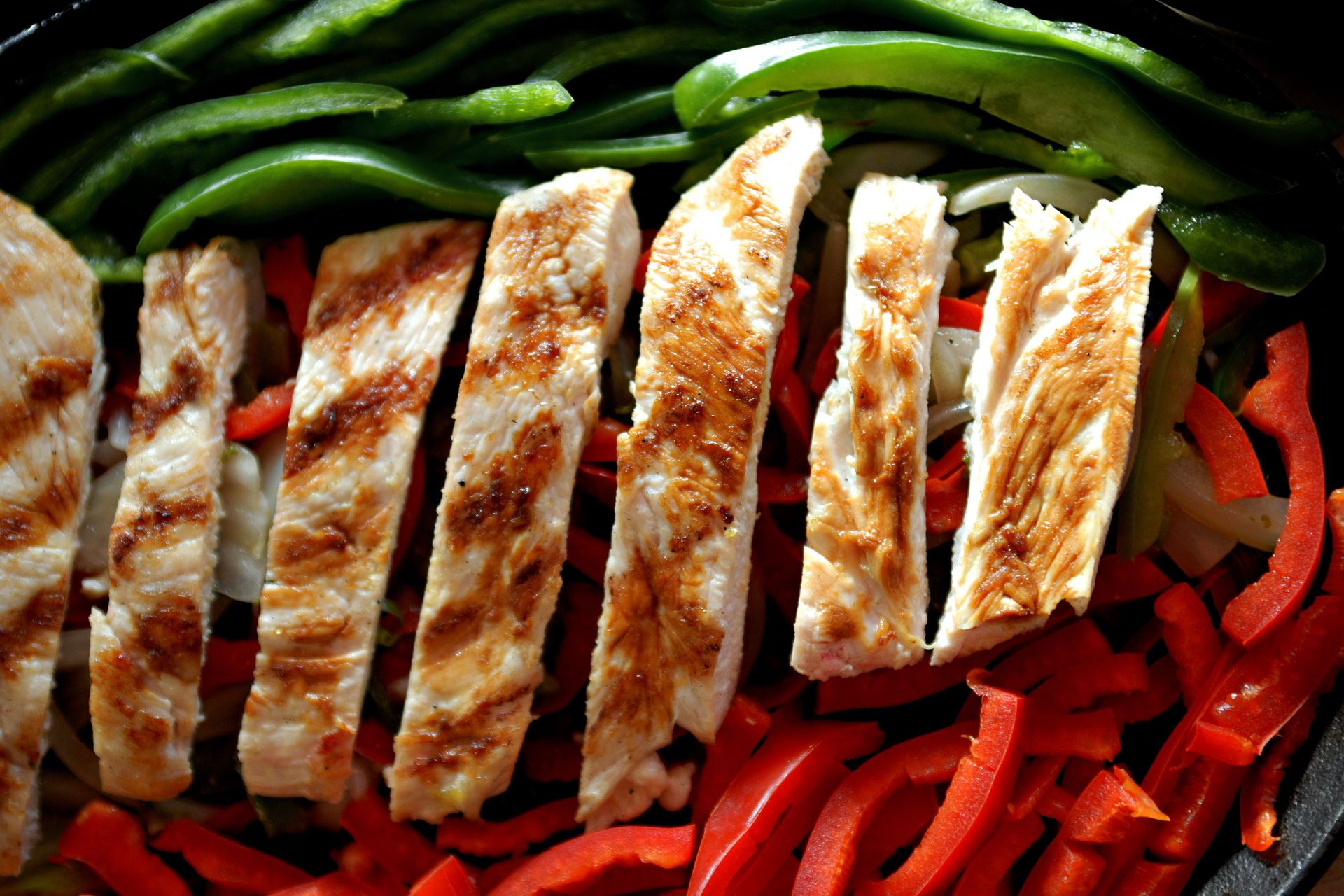 Sliced grilled chicken served with red and green peppers, perfect for fajitas.