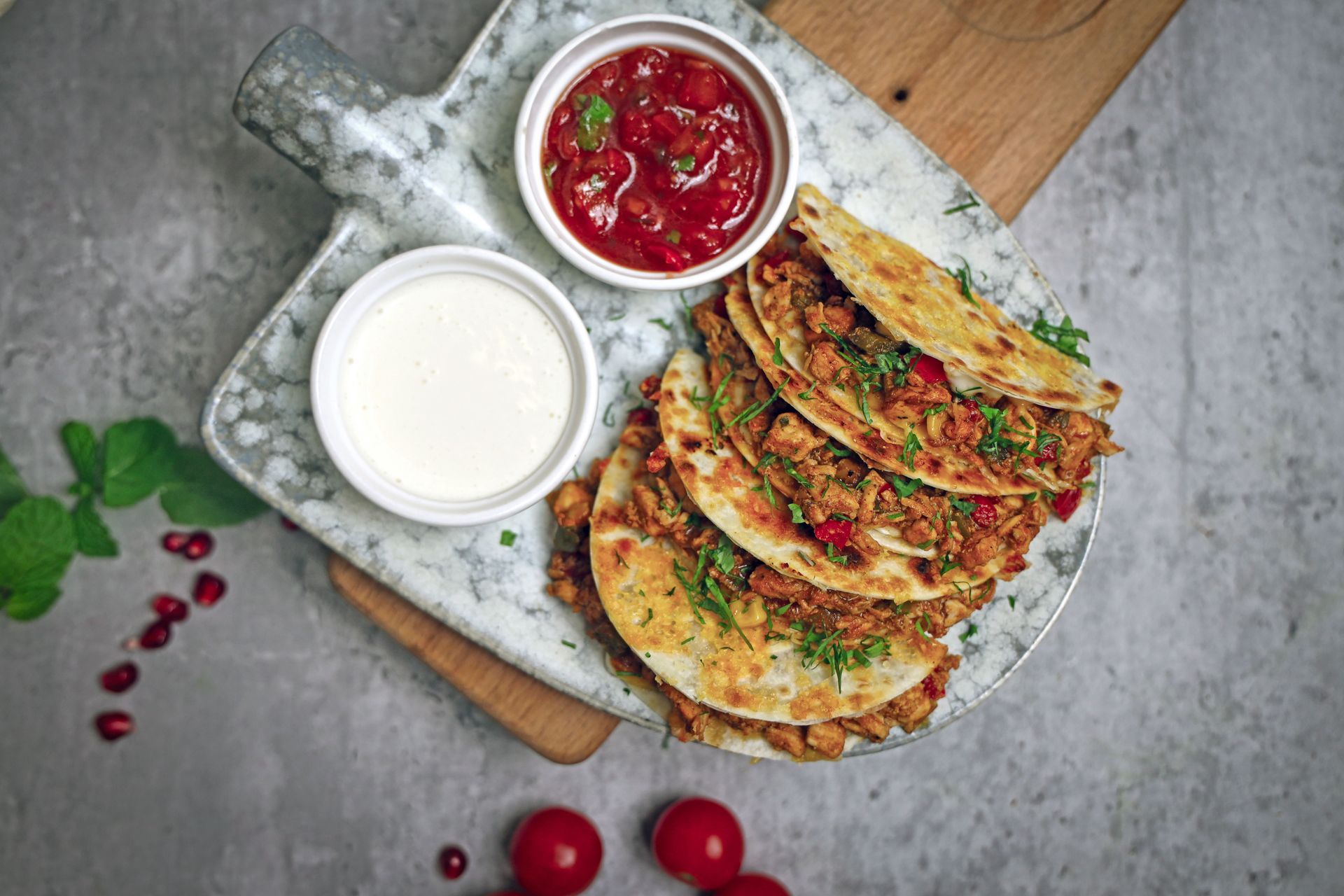 Top view of flavorful Mexican quesadillas served with salsa and cream dip on a marble plate.
