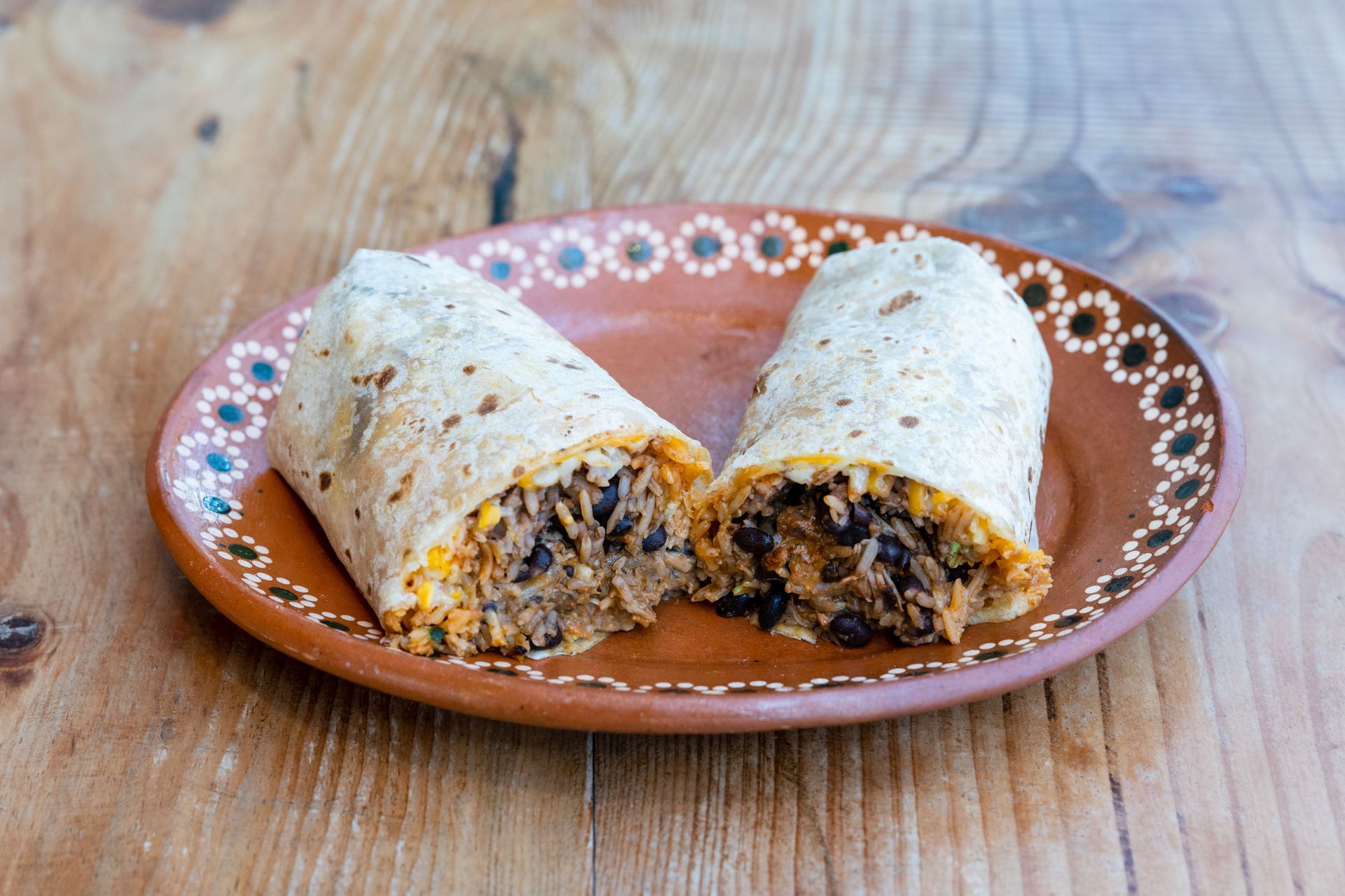 Close-up of a delicious Mexican burrito filled with rice, beans, and cheese on a decorative plate.