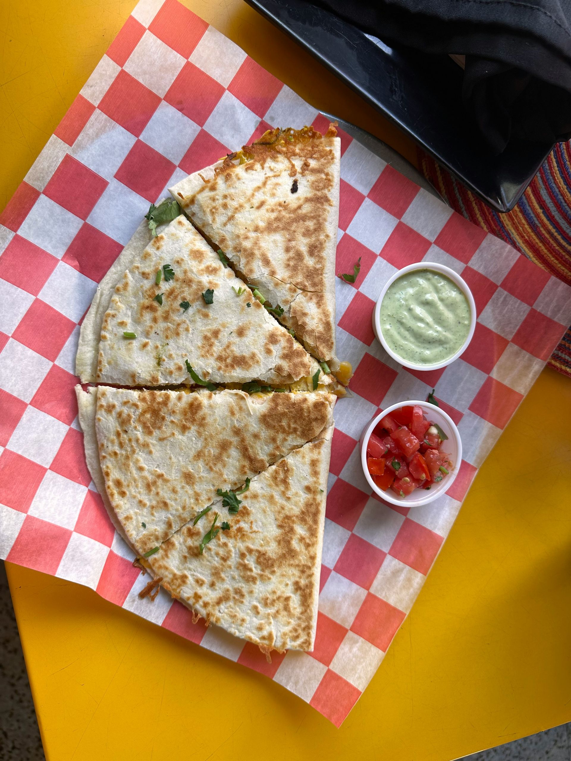 A quesadilla cut in half on a red and white checkered paper